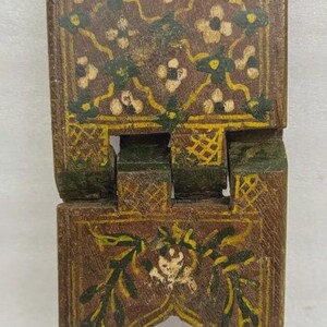 Puede incluir: Un peque&ntilde;o soporte de madera plegable con base marr&oacute;n y dise&ntilde;os florales intrincados en blanco, verde y amarillo. El soporte est&aacute; pintado con un patr&oacute;n detallado y tiene un arco decorativo en la base.