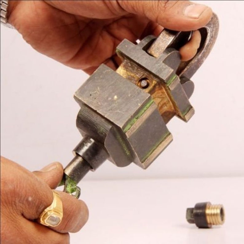 May include: A close-up of a metal tool with a green and black finish. The tool is being held by a person's hand and is being used to tighten a metal object. The object is a small, round, metal piece with a threaded end.