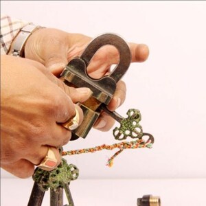 May include: A brass padlock with a decorative key, the padlock is open and the key is in the lock. The key is attached to a colourful string.
