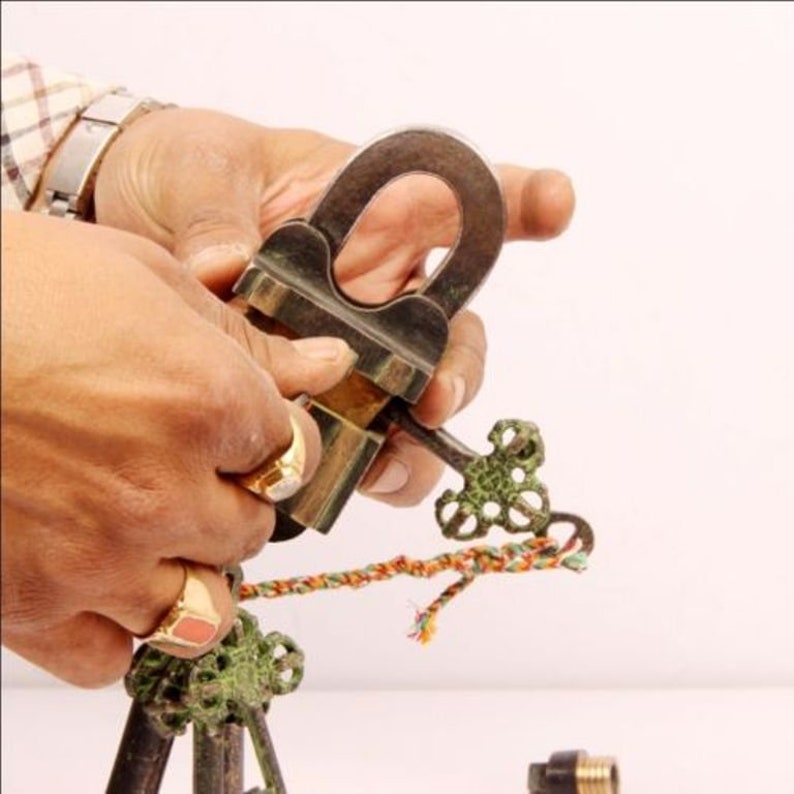 May include: A brass padlock with a decorative key, the padlock is open and the key is in the lock. The key is attached to a colourful string.