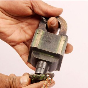 May include: A vintage brass padlock with a green patina and a key attached. The padlock has a square body with a rounded top and a keyhole on the side.