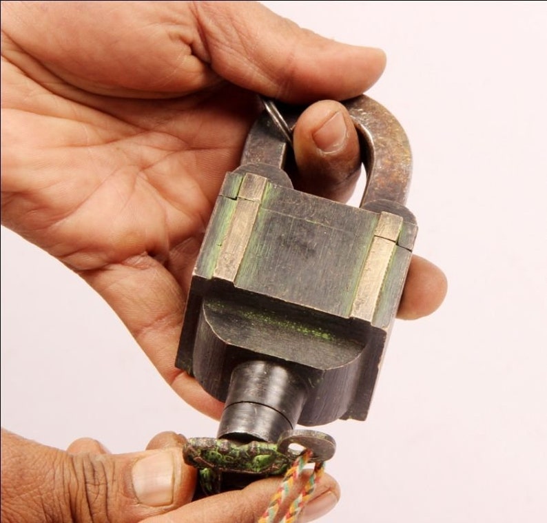 May include: A vintage brass padlock with a green patina and a key attached. The padlock has a square body with a rounded top and a keyhole on the side.