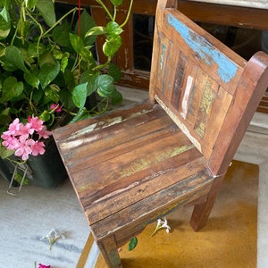 Puede incluir: Una silla de madera r&uacute;stica con un acabado desgastado. La silla es de color marr&oacute;n claro con acentos azules, verdes y amarillos. La silla est&aacute; hecha de madera recuperada y tiene un aspecto &uacute;nico y artesanal.