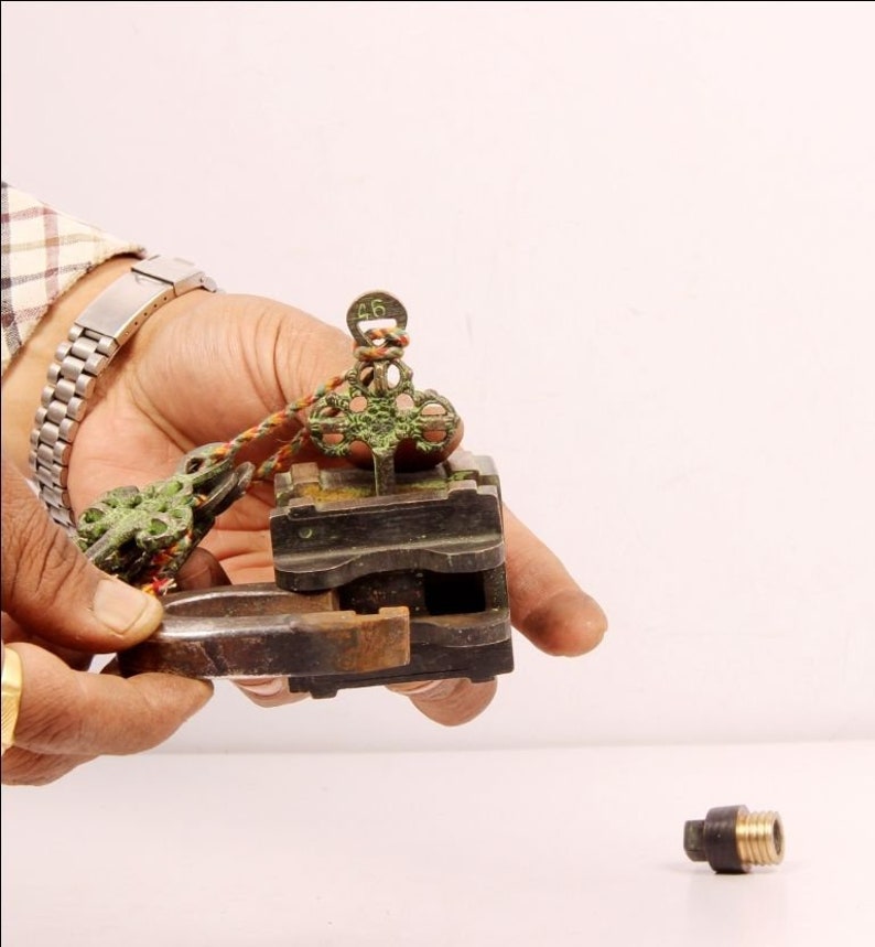 May include: A close-up of a vintage brass lock with a key and a small metal piece. The lock is green and has the number "46" on it. The lock is being held by a hand.