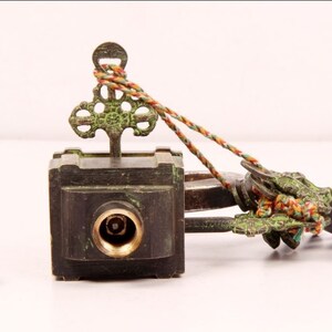 May include: A brass key with an ornate design and a green patina. The key is attached to a small, square box with a keyhole. The box is also made of brass and has a green patina. The key and box are connected by a string.