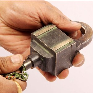 May include: A vintage brass padlock with a key. The padlock has a square body with a rounded top and a metal loop on the side. The key is ornate and has a green patina.