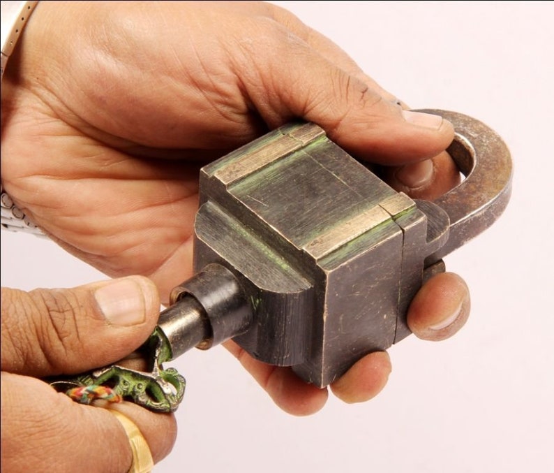 May include: A vintage brass padlock with a key. The padlock has a square body with a rounded top and a metal loop on the side. The key is ornate and has a green patina.
