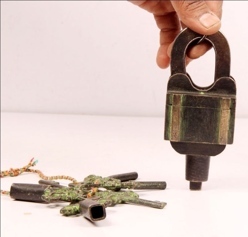 May include: A vintage brass padlock with a green patina and a set of five ornate keys. The keys are attached to a colourful string.