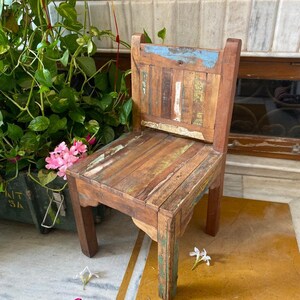 Puede incluir: Una silla de madera r&uacute;stica con un respaldo y un asiento de patchwork multicolor. La silla tiene un acabado desgastado y est&aacute; hecha de madera reciclada.