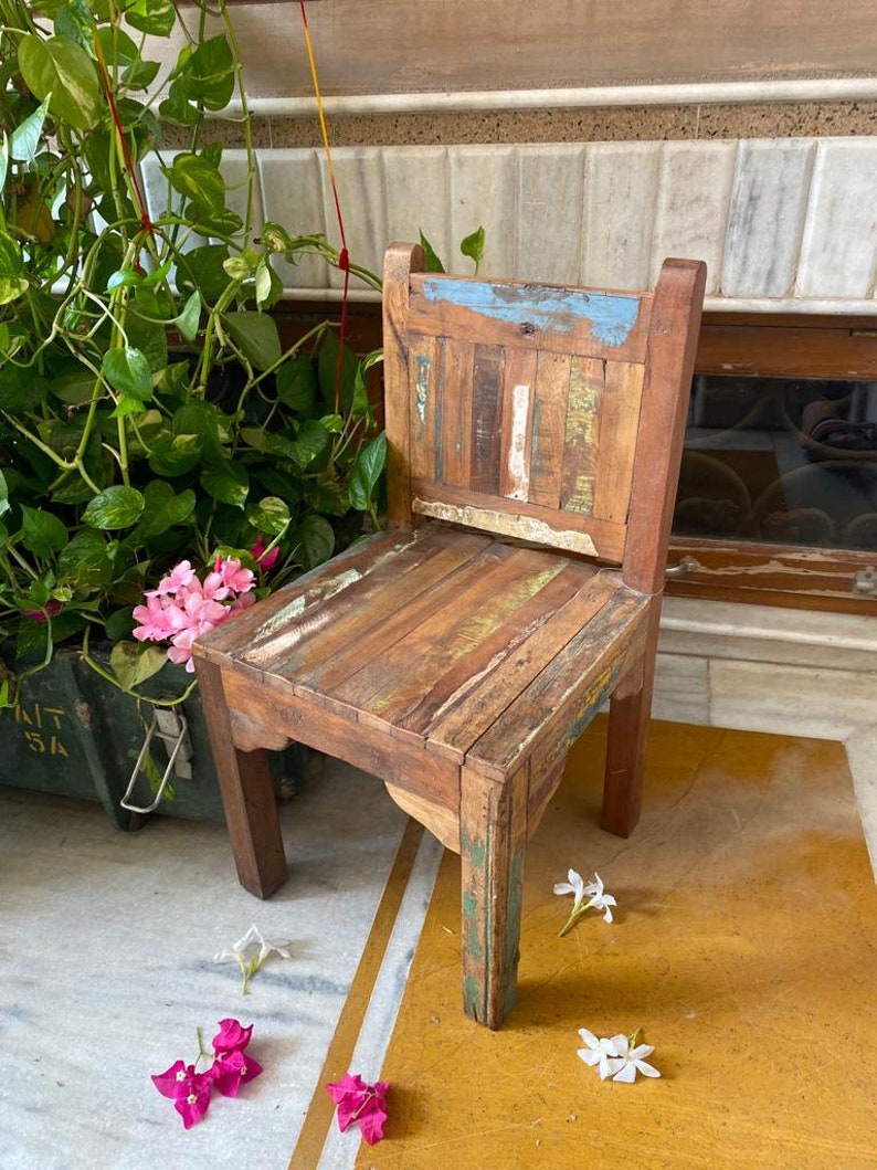 Puede incluir: Una silla de madera r&uacute;stica con un respaldo y un asiento de patchwork multicolor. La silla tiene un acabado desgastado y est&aacute; hecha de madera reciclada.
