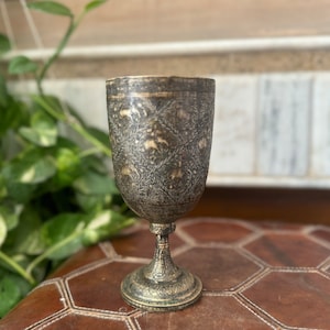 May include: A silver goblet with an intricate floral and geometric design. The goblet has a wide base and a tall, slender stem.