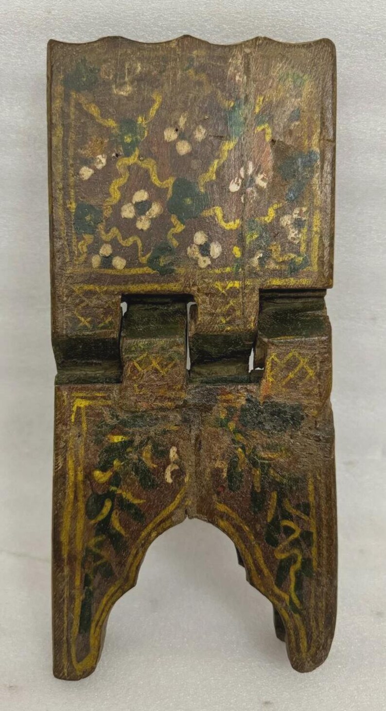 Puede incluir: Un peque&ntilde;o atril de madera con bisagras y acabado envejecido. El atril est&aacute; pintado con motivos florales y de vid en amarillo, verde y blanco sobre un fondo marr&oacute;n. Dise&ntilde;ado para sostener un libro en posici&oacute;n vertical.
