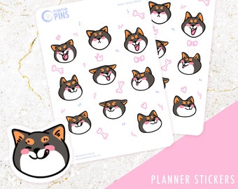 Op de afbeelding: Twee vellen met planner stickers met Shiba Inu honden gezichten met verschillende uitdrukkingen. De stickers zijn op een witte achtergrond met roze, blauwe en zwarte accenten. De tekst "Pompom Pins" en "Planner Stickers" is zichtbaar op de vellen.