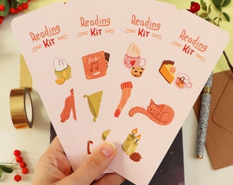 Op de afbeelding: Vier roze bladwijzers met de tekst "Reading Kit" en verschillende illustraties, waaronder een kat, kaarsen, een boek en een kopje koffie. 