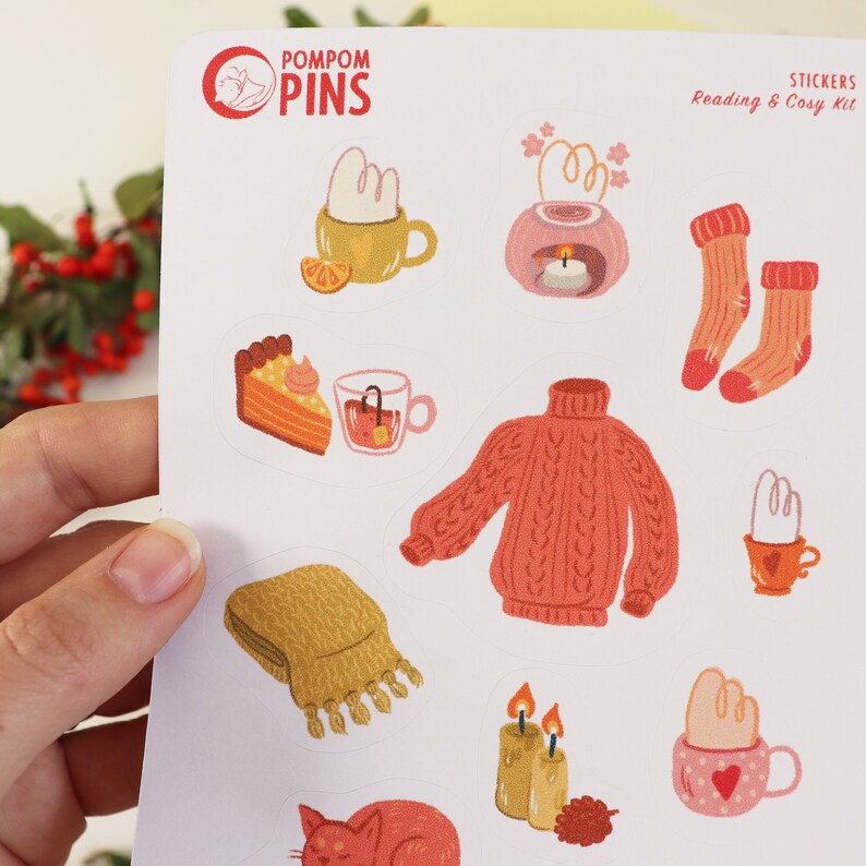 Op de afbeelding: Een vel stickers met een knus winterthema. De stickers bevatten illustraties van een warme trui, een mok met warme chocolademelk, een stuk taart, een kaars, een kat en een sjaal. De stickers zijn perfect om een ​​beetje warmte en comfort toe te voegen aan je planner, dagboek of laptop.