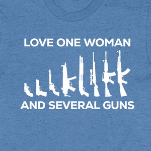 May include: A blue t-shirt with white text that reads "Love one woman and several guns". The text is surrounded by a row of white silhouette images of guns.