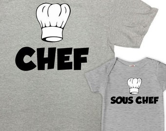 Könnte beinhalten: Ein graues T-Shirt mit einer schwarzen Kochmütze und dem Wort "CHEF" darauf gedruckt. Ein grauer Baby-Strampler mit einer schwarzen Kochmütze und dem Wort "SOUS CHEF" darauf gedruckt.