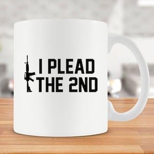 May include: White ceramic coffee mug with a black silhouette of a rifle and the text "I PLEAD THE 2ND".