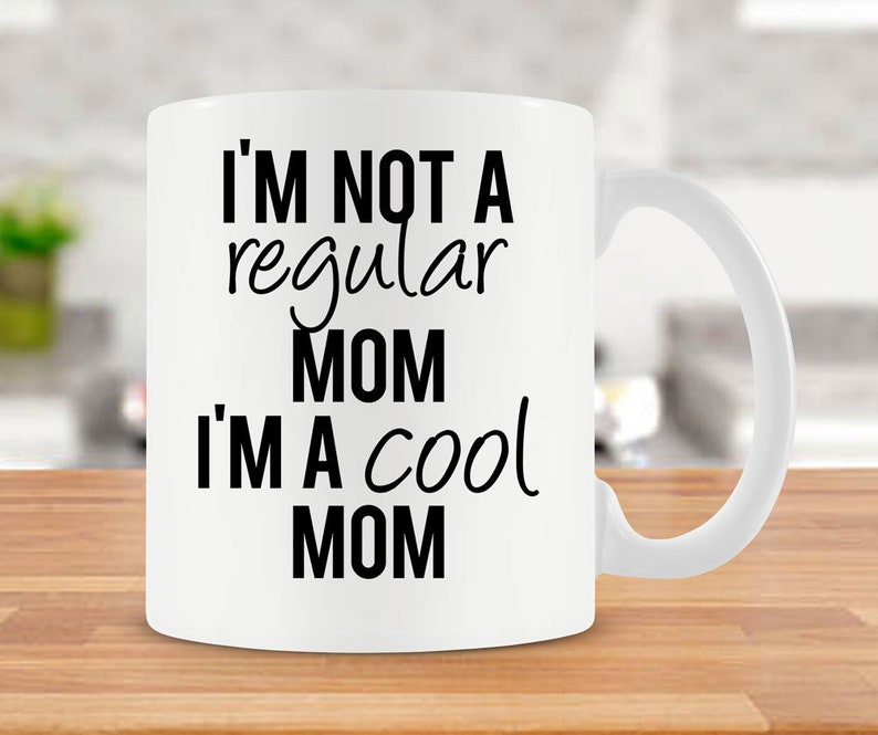 May include: White ceramic coffee mug with black text that reads "I'm not a regular mom I'm a cool mom".