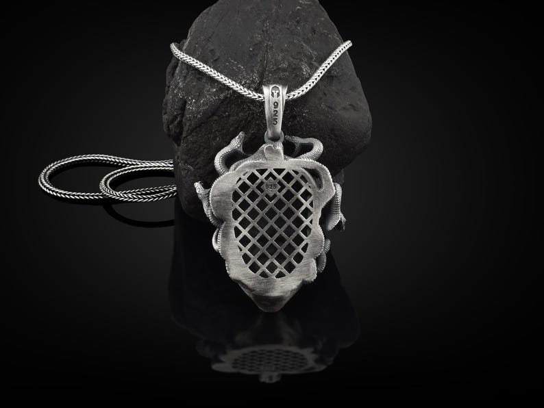 May include: A silver necklace with a detailed pendant featuring a heart-shaped design with a lattice pattern. The pendant is surrounded by a snake-like design.