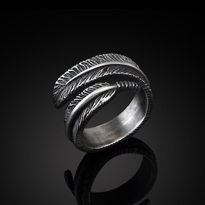以下が含まれることがあります： 羽根の模様が細かく刻まれた銀の指輪。指輪は金属製で、質感のある仕上げになっています。