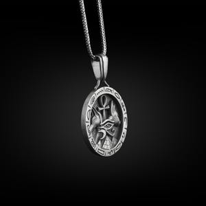 Pu&ograve; includere: Collana con ciondolo in argento con un design intricato che presenta un occhio, due teste di animali e un simbolo ankh. Il ciondolo &egrave; circondato da un cerchio di geroglifici.