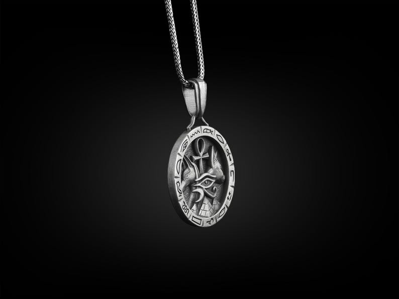 Pu&ograve; includere: Collana con ciondolo in argento con un design intricato che presenta un occhio, due teste di animali e un simbolo ankh. Il ciondolo &egrave; circondato da un cerchio di geroglifici.