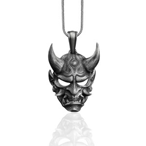 May include: Silver pendant necklace featuring a detailed, silver-toned oni mask with horns, a fierce expression, and intricate details.