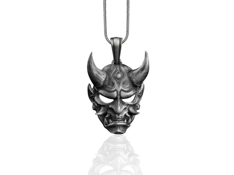 May include: Silver pendant necklace featuring a detailed, silver-toned oni mask with horns, a fierce expression, and intricate details.