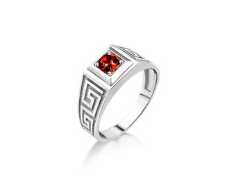 Könnte beinhalten: Ein silberner Ring mit einem roten Edelstein, der in einer quadratischen Fassung sitzt. Der Ring hat ein geometrisches Design auf der Band.