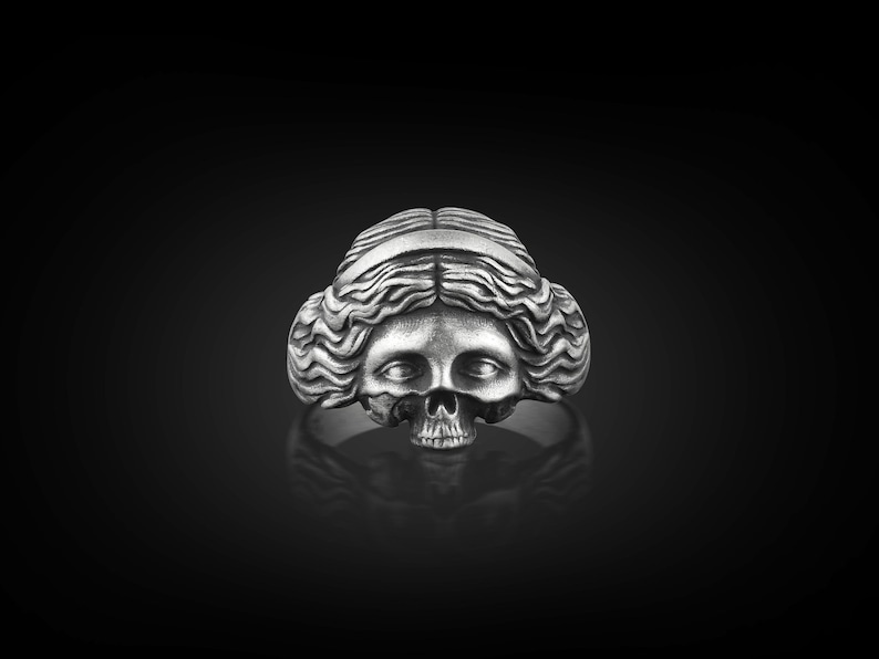May include: A silver ring with a detailed skull design, featuring a woman's face with long hair.