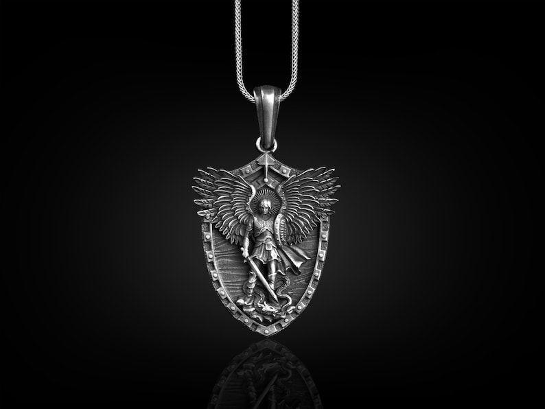 Puede incluir: Collar con colgante de plata con un escudo con un &aacute;ngel que sostiene una espada y un drag&oacute;n. El &aacute;ngel tiene alas y lleva armadura. El escudo est&aacute; detallado con una superficie texturizada.