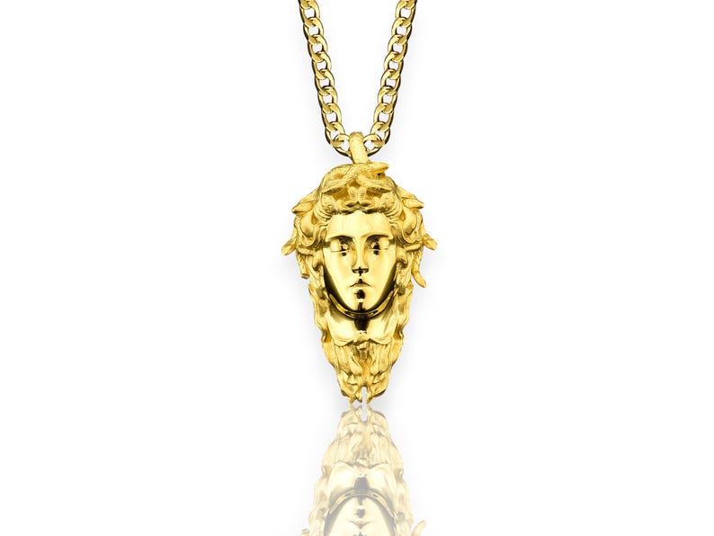 May include: A gold chain necklace with a pendant featuring a detailed, three-dimensional depiction of Medusa's face.