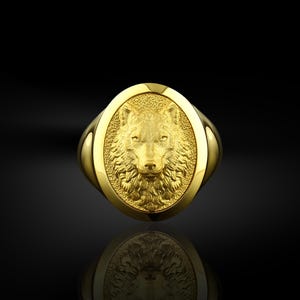 May include: A gold ring with an oval-shaped design featuring a detailed wolf head in relief.