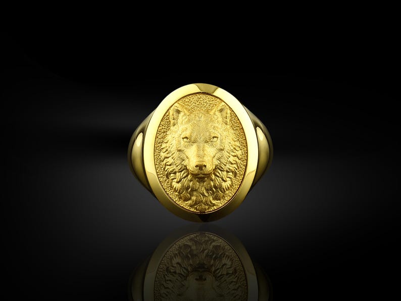 May include: A gold ring with an oval-shaped design featuring a detailed wolf head in relief.