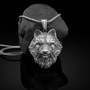 Könnte beinhalten: Silberner Wolfskopf-Anhänger mit detaillierter Textur, an einer passenden Kette. Der Wolf zeigt die Zähne. Das Schmuckstück wird vor dunklem Hintergrund präsentiert. Die Kette ist etwa 50 cm lang.