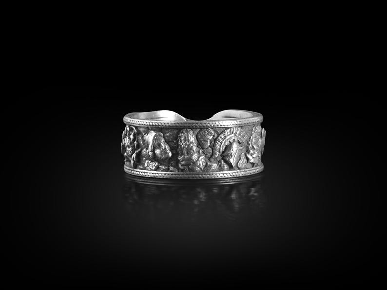 Pu&ograve; includere: Un anello d'argento con un design dettagliato di varie figure e simboli. L'anello &egrave; largo e ha una superficie testurizzata.