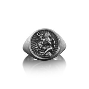 Puede incluir: Un anillo de sello de plata con un dise&ntilde;o detallado de un caballero a caballo matando a un drag&oacute;n.