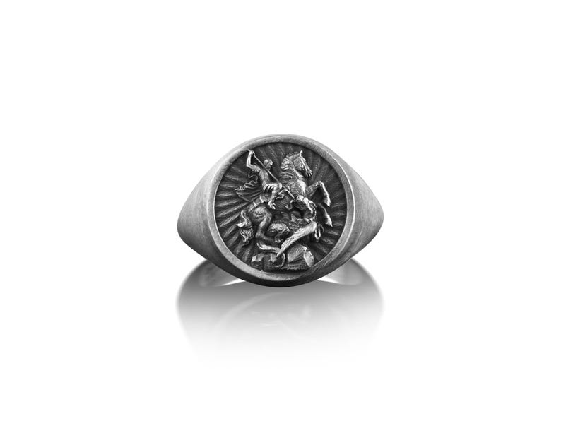 Puede incluir: Un anillo de sello de plata con un dise&ntilde;o detallado de un caballero a caballo matando a un drag&oacute;n.