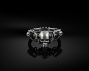 May include: A silver ring featuring a skull design. The skull is encircled by a twisted metal band.