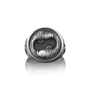 Peut inclure: Une bague en argent avec un motif d&eacute;taill&eacute; de deux poissons se faisant face dans un cercle.