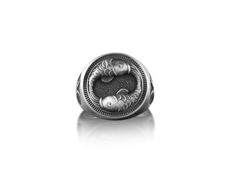 Peut inclure: Une bague en argent avec un motif d&eacute;taill&eacute; de deux poissons se faisant face dans un cercle.