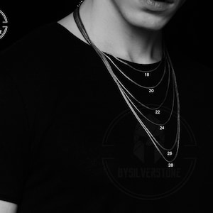 May include: A black and white image of a person wearing a black shirt with a silver chain necklace. The chain is shown in different lengths, labeled with numbers from 18 to 28.