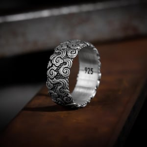 Può includere: Un anello d'argento con un design dettagliato di nuvole vorticose. L'anello è contrassegnato con "925" sulla fascia interna.