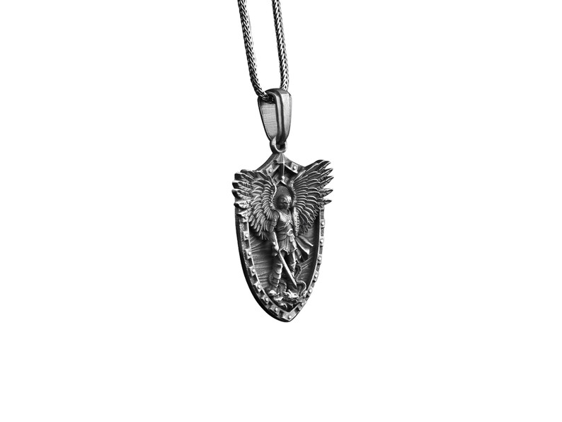 Puede incluir: Collar con colgante de plata que presenta un escudo con un &aacute;ngel que sostiene una espada. El &aacute;ngel tiene alas y est&aacute; representado en un dise&ntilde;o detallado en tres dimensiones.