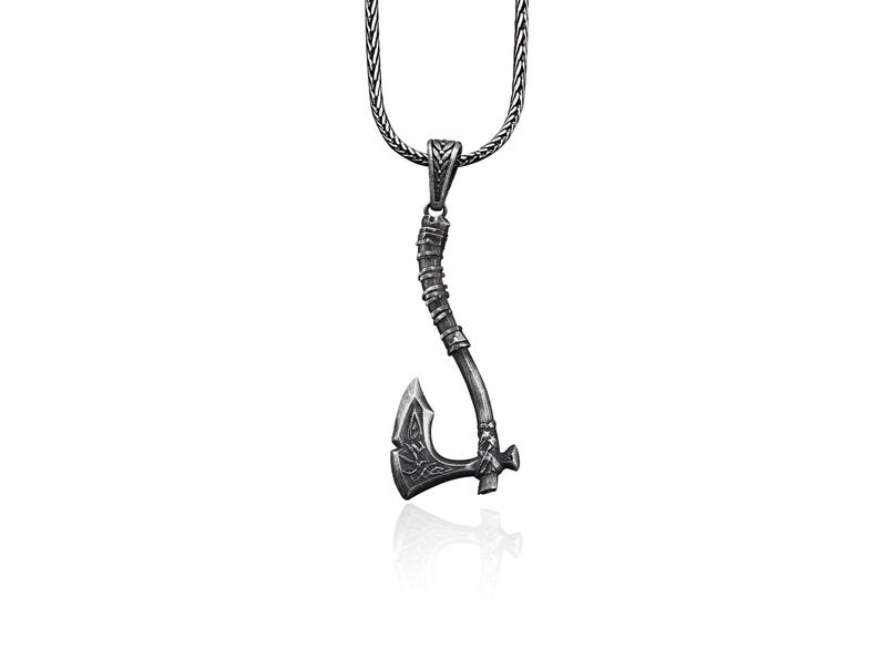May include: A silver necklace with a pendant shaped like an axe. The axe has a detailed design and a textured handle.