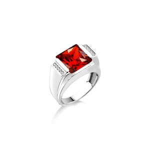 Peut inclure: Bague en argent ornée d'une grande pierre rouge rectangulaire à facettes. La bague a une finition polie et est ornée de petits diamants clairs de chaque côté de la pierre principale. Design classique et audacieux.