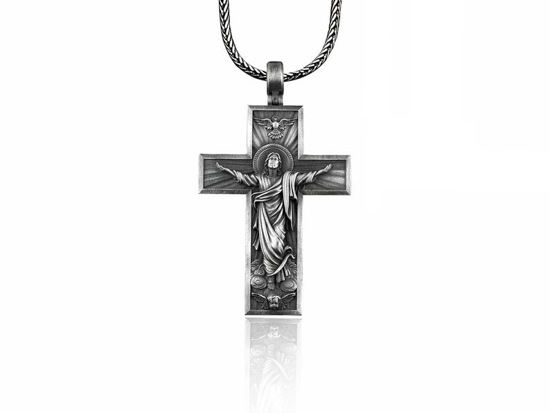 May include: Silver pendant necklace featuring a detailed cross with a depiction of Jesus Christ. The cross has a raised design and a textured finish.