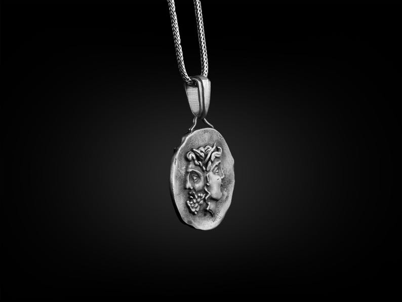 May include: A silver necklace with a pendant featuring two faces in profile. The pendant is round and has a textured surface.
