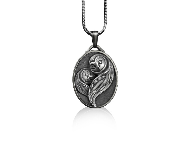 May include: A silver pendant necklace featuring two owls in a heart shape. The owls are intricately detailed and have a realistic appearance.